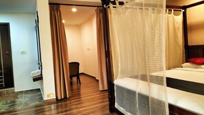 A hotel room with a four-poster bed, wooden flooring, a chair, and a small desk. - Hotel Bright Heritage (Kochi)
