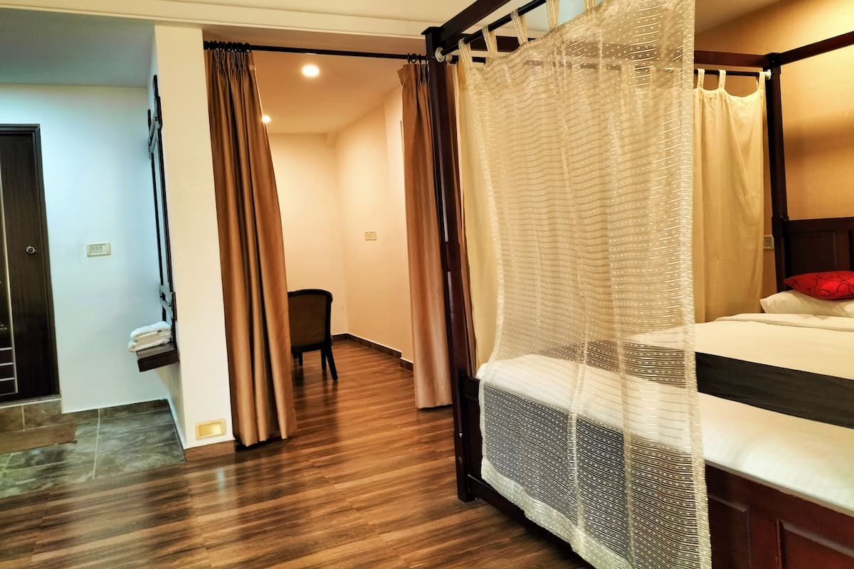 A hotel room with a four-poster bed, wooden flooring, a chair, and a small desk.