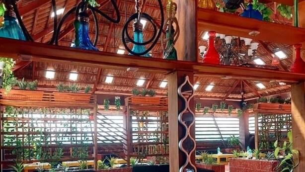 A restaurant with wooden beams, hanging plants, and a variety of colorful hookahs. - Hotel Bright Heritage (Kochi)