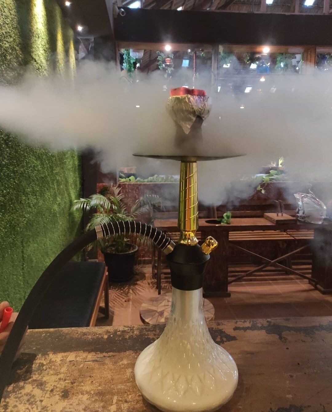 Un narguile con base blanca y tallo dorado, que exhala humo.