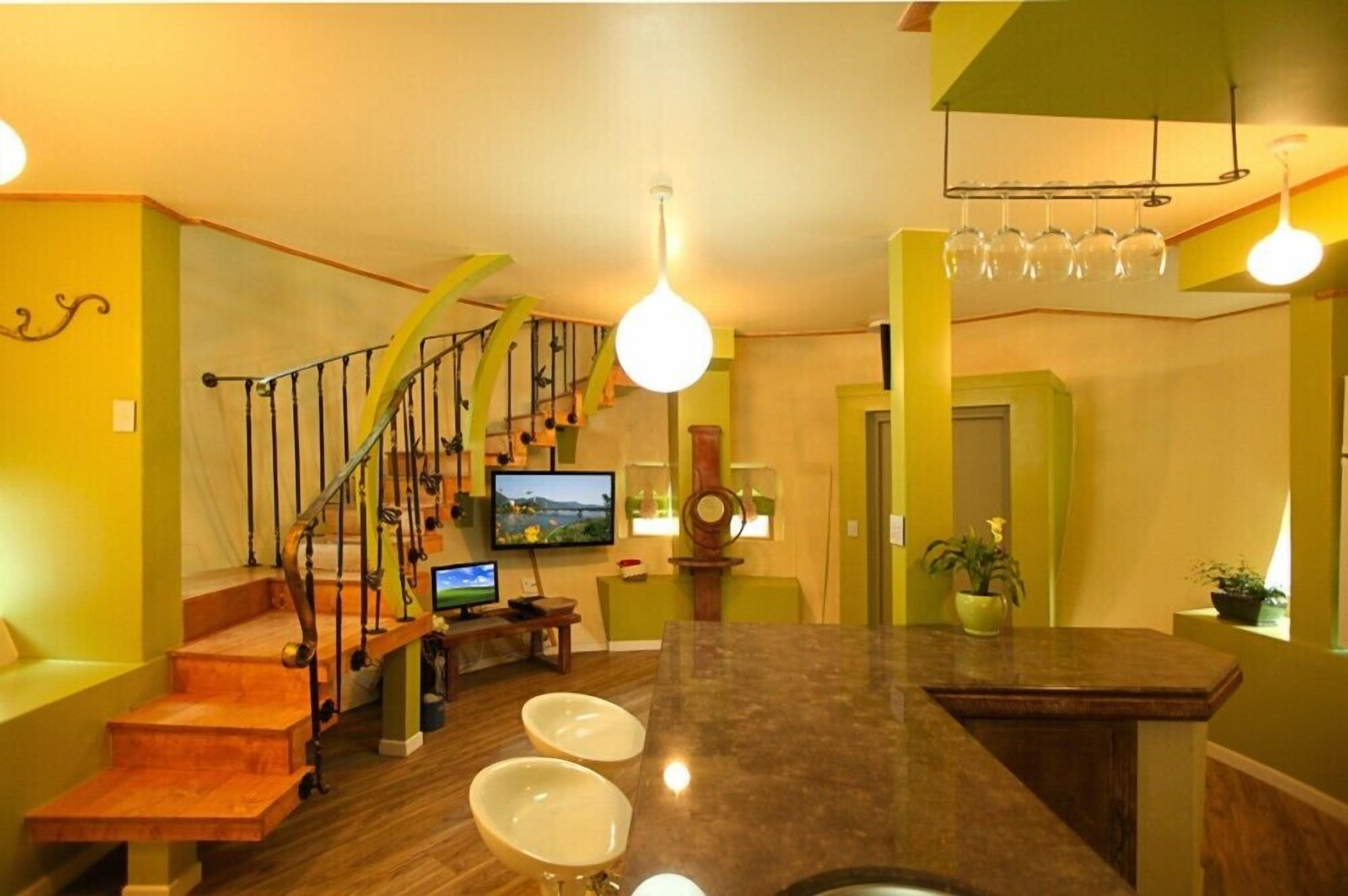 A modern kitchen with a wooden staircase, a dining area with bar stools, and a TV mounted on the wall.