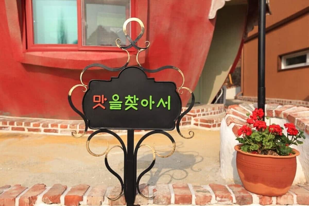 A black sign with Korean text, a potted red flower, and a brick wall.