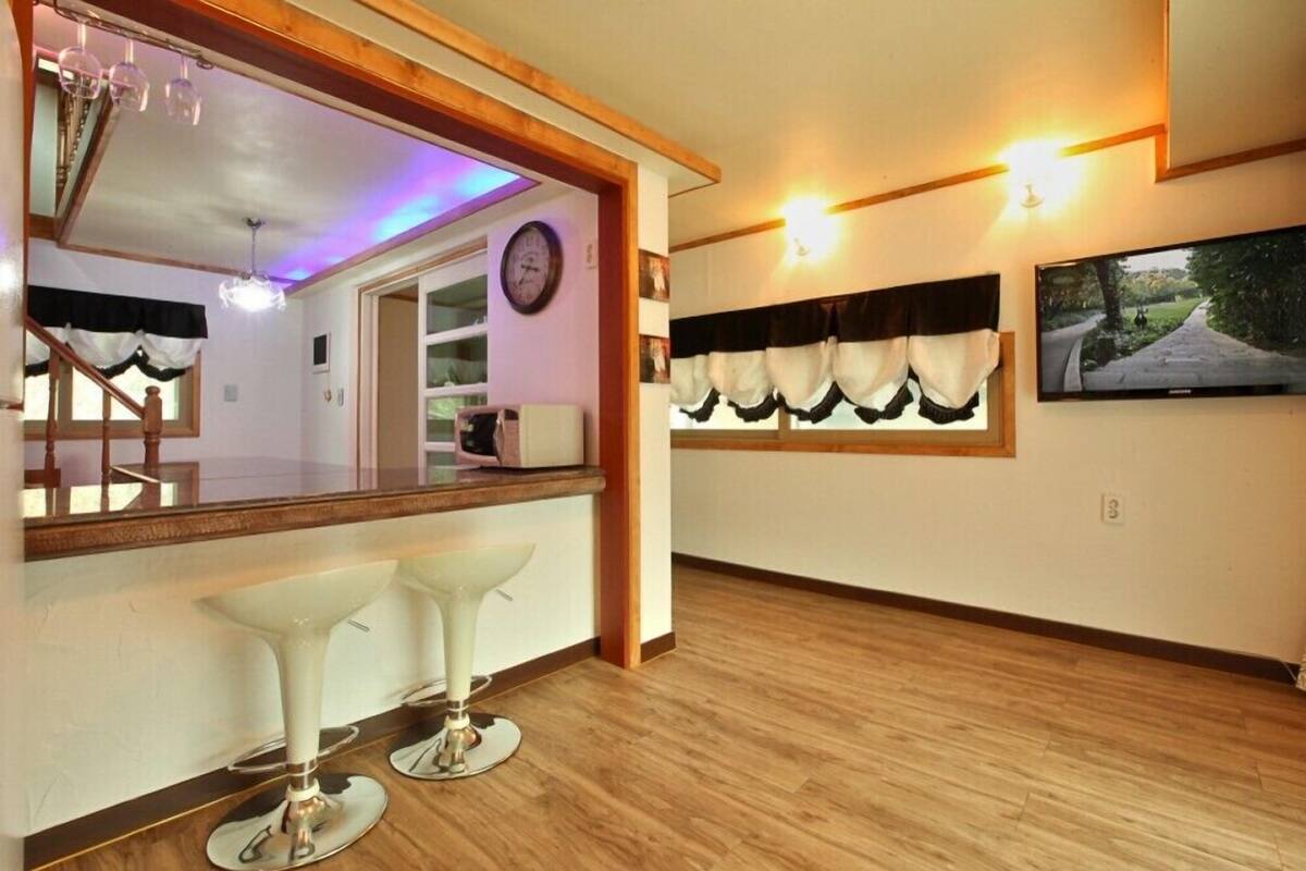 A spacious room with a large mirror, two bar stools, a wooden floor, a staircase, and a wall-mounted TV.