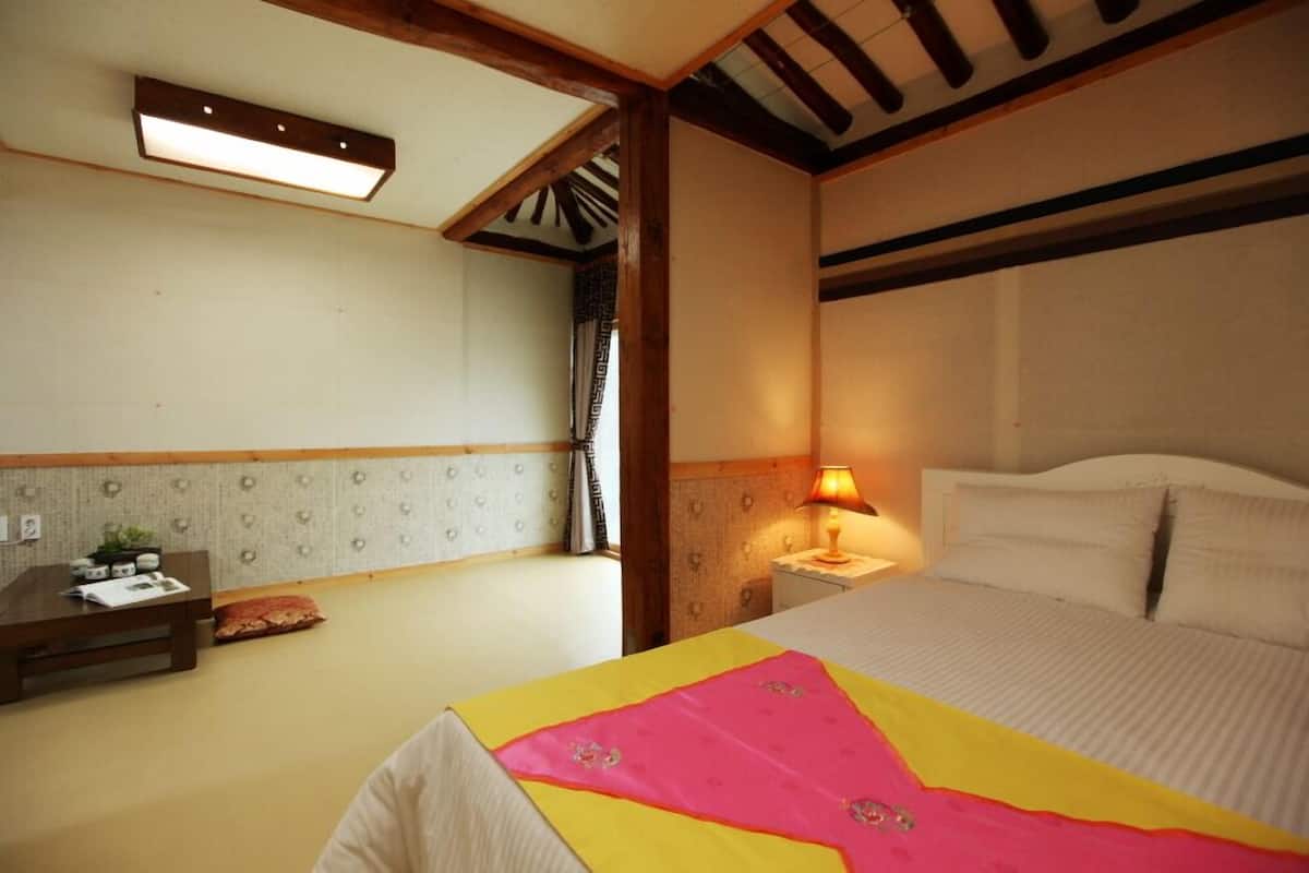 A hotel room with a bed, bedside table, lamp, and a small desk with a chair.
