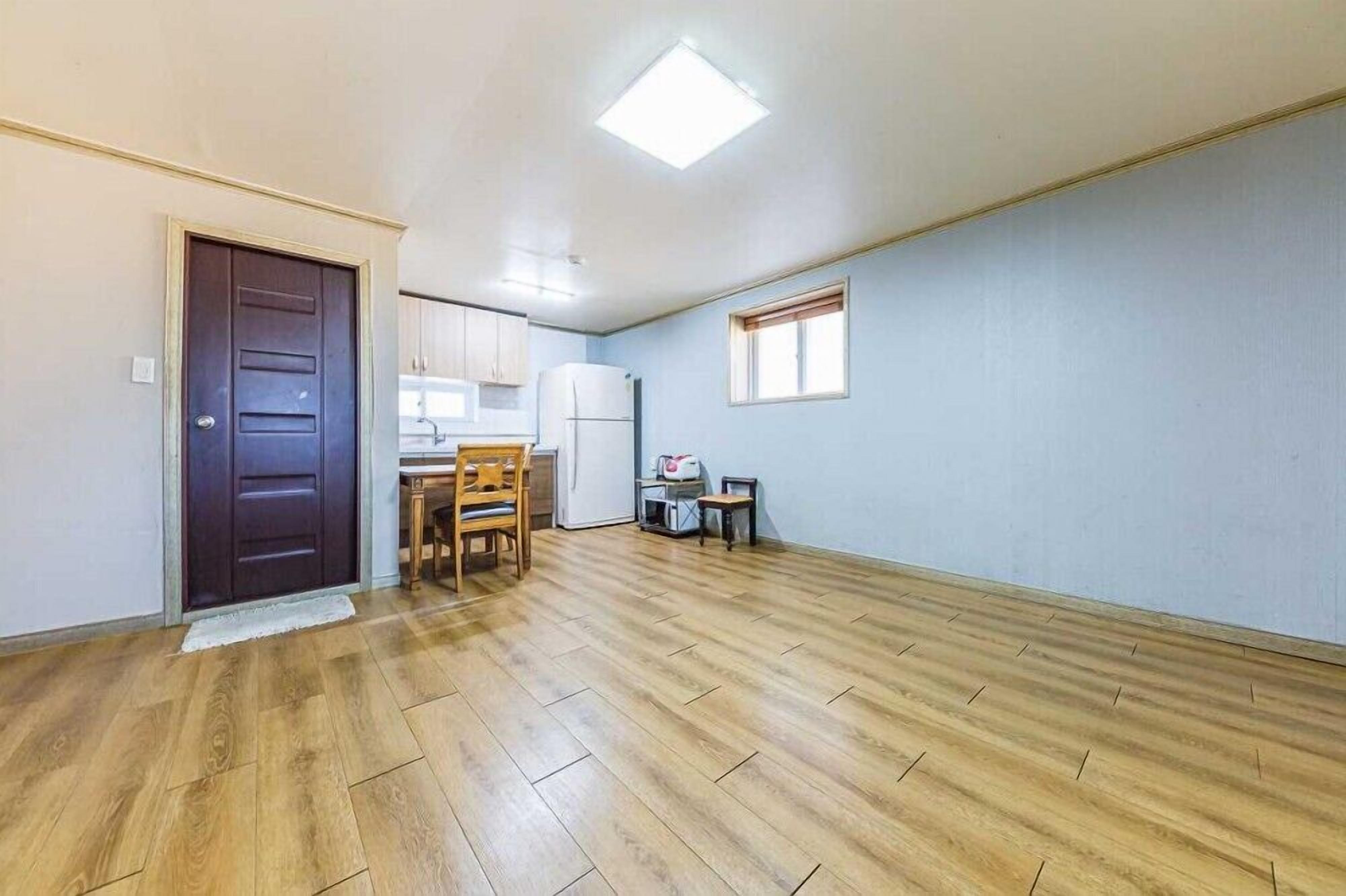 Um quarto espaçoso com piso de madeira, área de jantar com mesa e cadeiras, geladeira e janela com persianas.