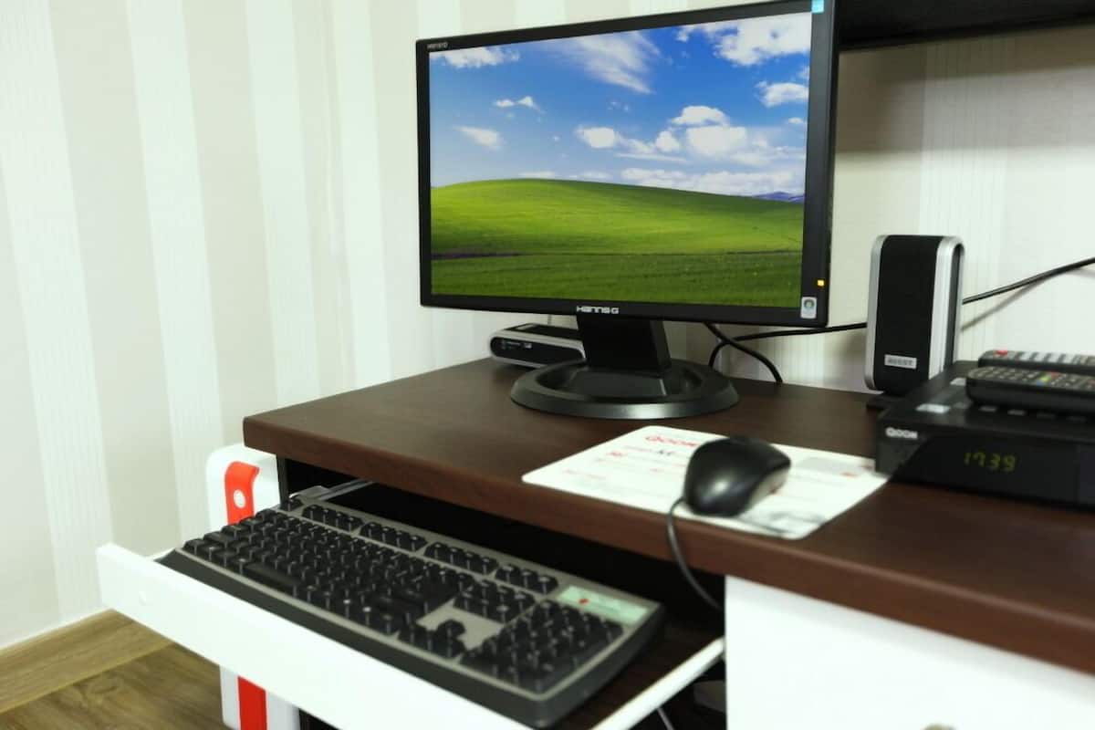 A computer desk with a monitor, keyboard, mouse, and a small speaker.