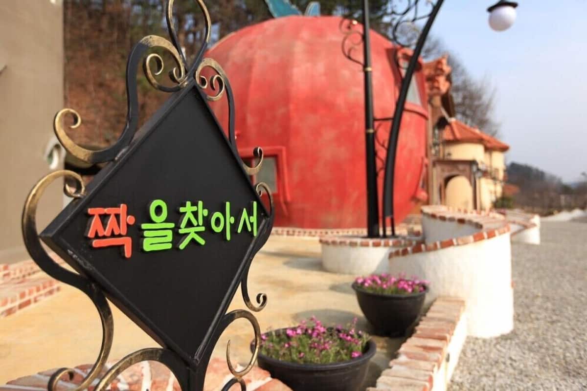 A black metal sign with Korean text, a red spherical structure, and potted plants in a courtyard.