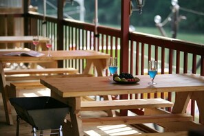 A wooden deck with tables and benches, a wheelbarrow, and a glass of blue cocktail.