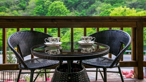 A round table with two chairs on a wooden deck, overlooking a lush green forest. - Eco Pia Pension (Gapyeong)