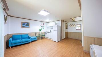 Un espacio habitable compacto con un sofá azul, una pequeña mesa de comedor con sillas, una kitchenette y piso de madera.