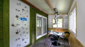 A room with a wooden floor, a table with chairs, a window, and a door with a number sign.