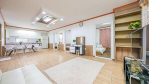 A spacious living area with a kitchen, a dining table with chairs, a sofa, a small desk with a chair, and a bed with a pink curtain. - Eco Pia Pension (Gapyeong)