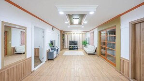 A spacious living room with a large TV, a sofa, and a sliding glass door leading to a balcony. - Eco Pia Pension (Gapyeong)