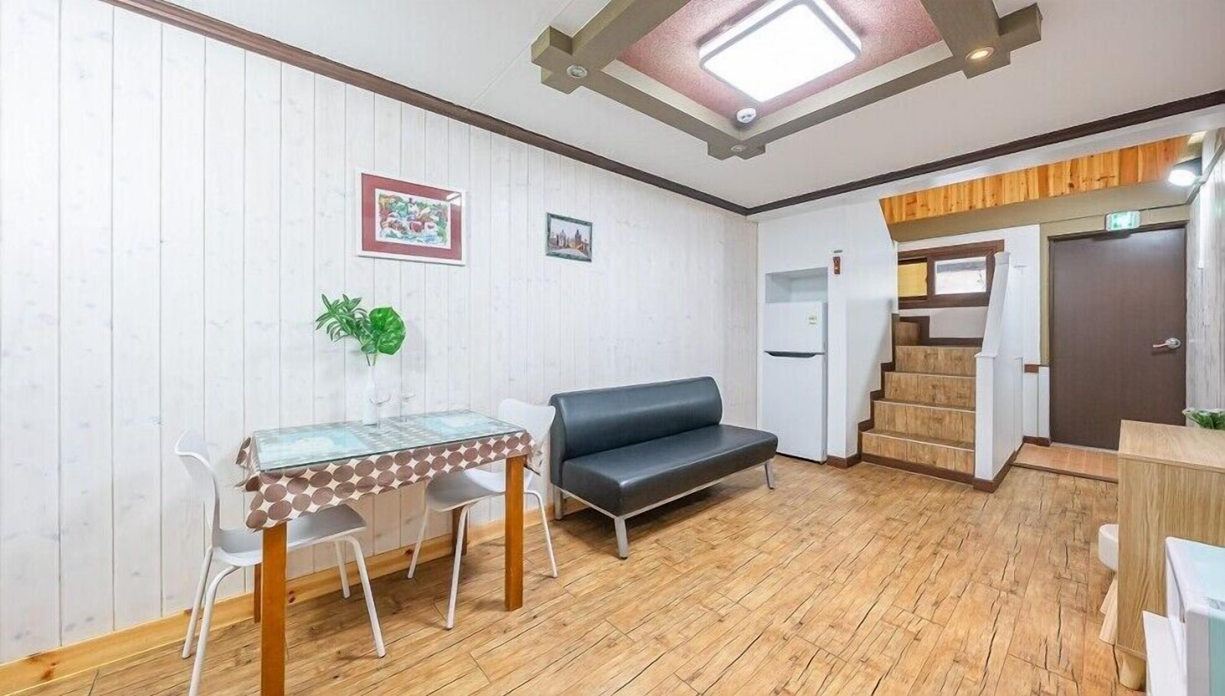 A compact living space with a dining area, a sofa, a staircase, and a door leading to another room.
