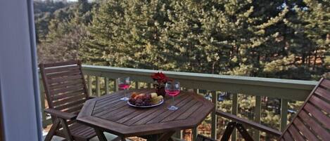 Una mesa de madera con un plato de fruta y dos vasos en un balcón con vista a un bosque.
