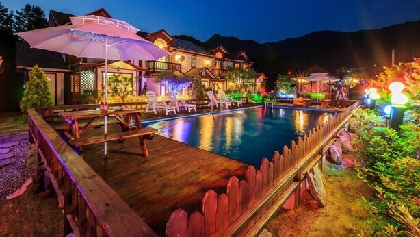 A swimming pool with a wooden deck and lounge chairs, surrounded by a wooden fence and a gazebo.