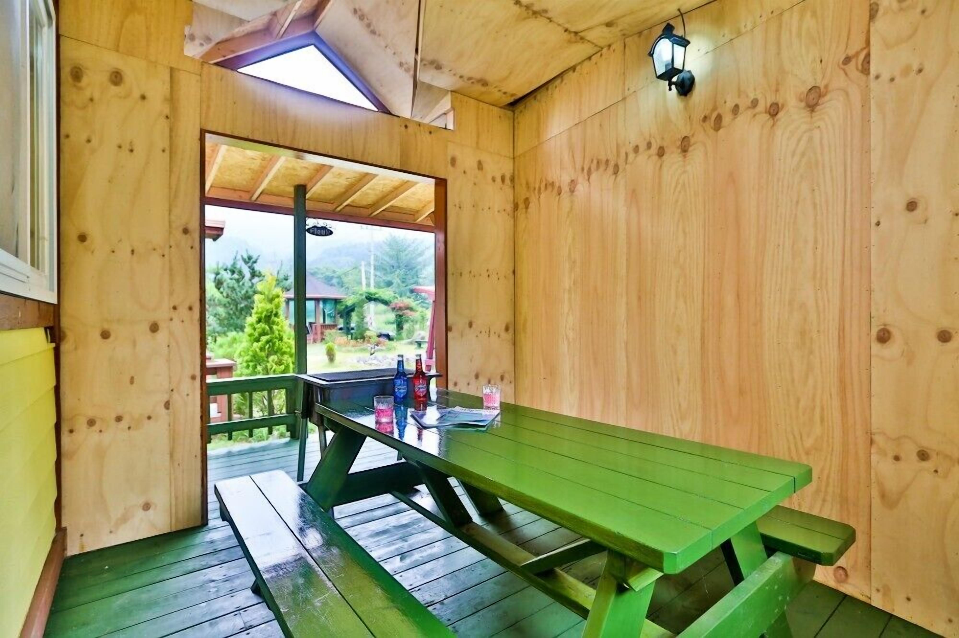 Une cabane en bois avec une table de pique-nique et des bancs, une porte vitrée donnant sur l’extérieur et une lanterne fixée au mur.