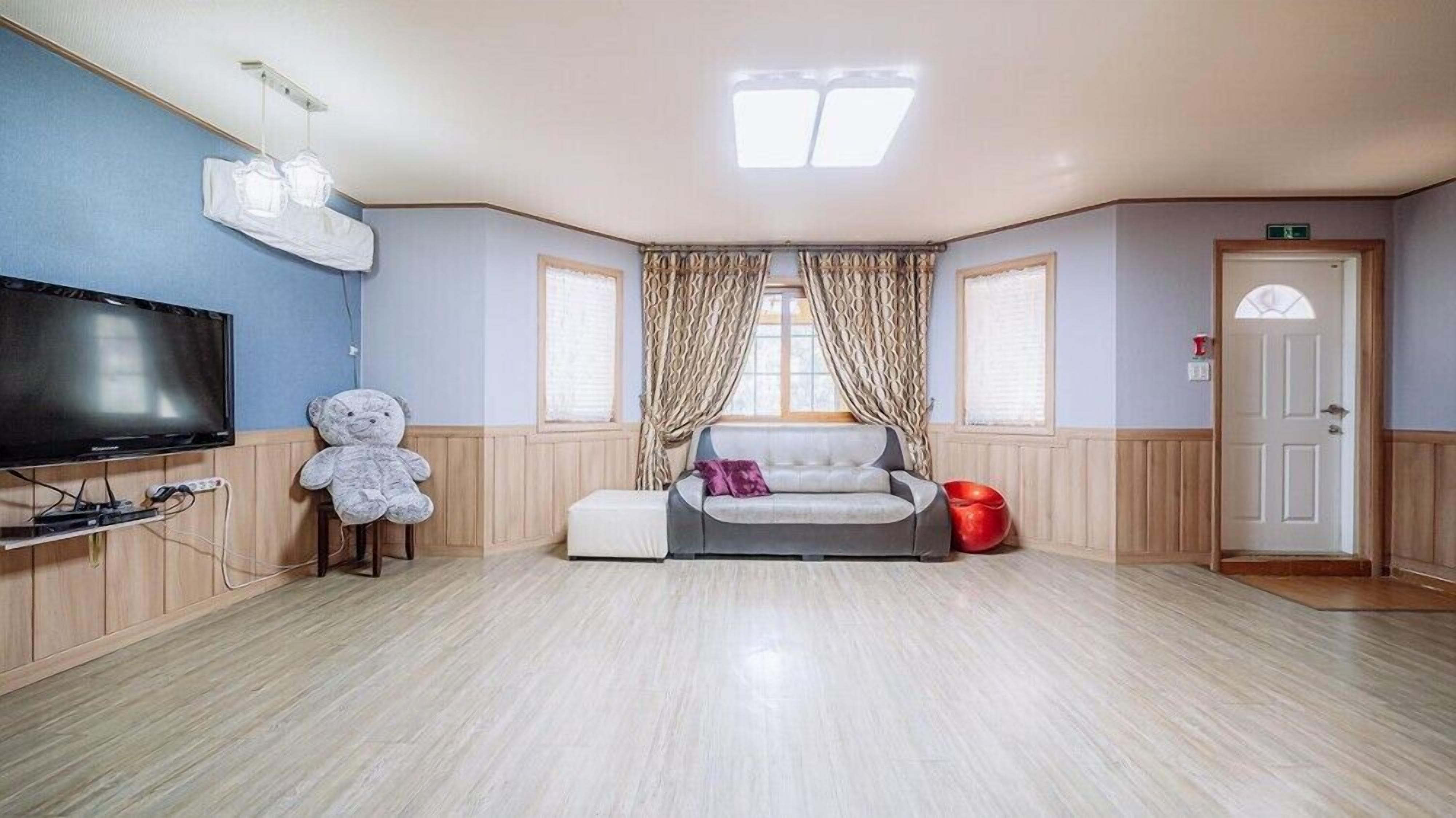 A spacious room with a flat-screen TV, a large teddy bear, a grey sofa, and a red chair.