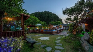 A garden with stone pathways, wooden structures, and outdoor seating areas.