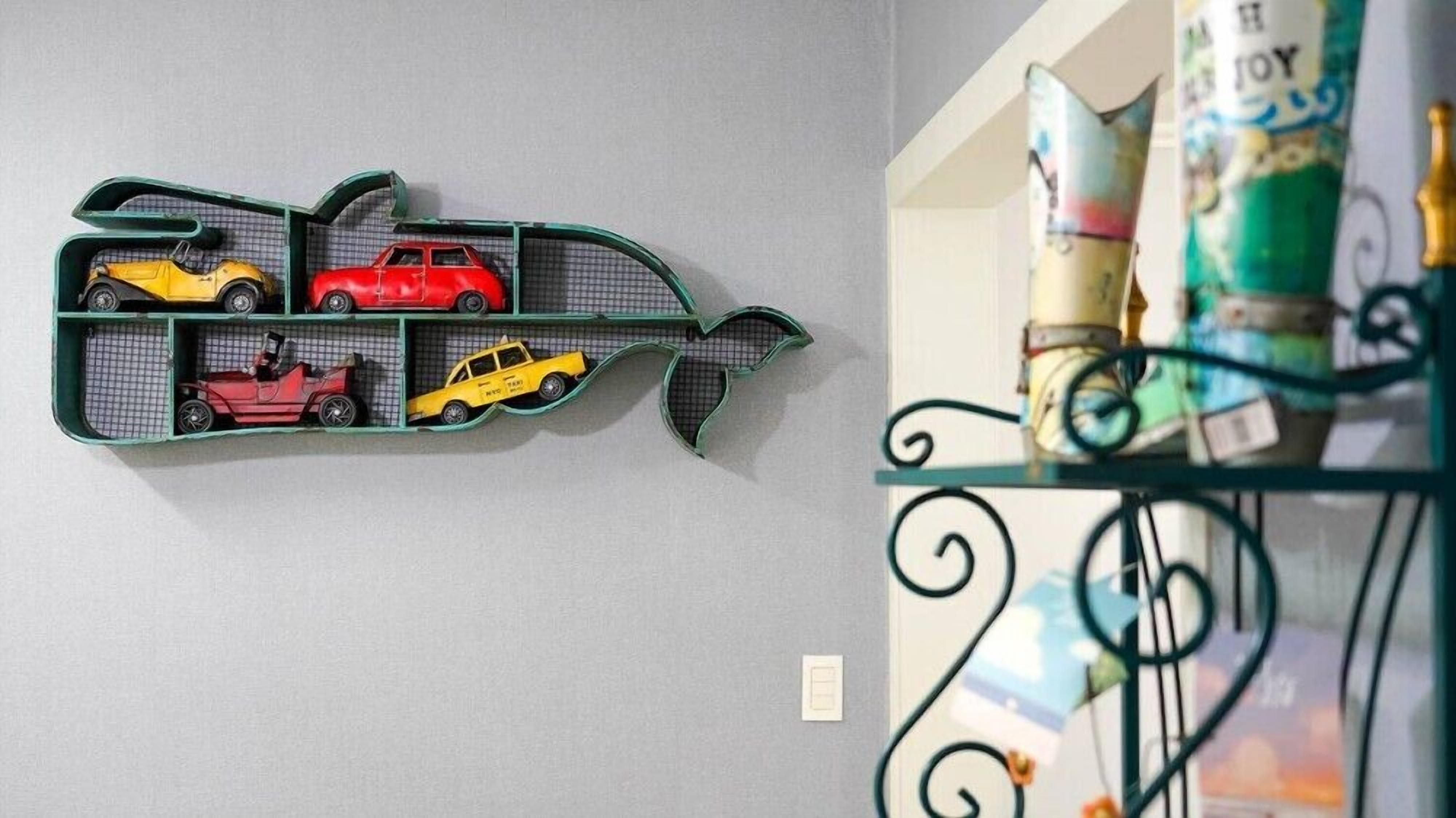 Un estante montado en la pared con coches de juguete y una estructura decorativa con forma de pez.
