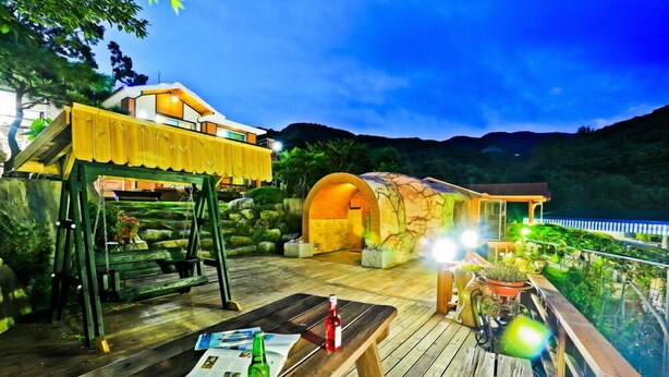 A wooden deck with a table, a swing, and a covered seating area with a view of the mountains. - Sambatgol Pension (Pocheon)