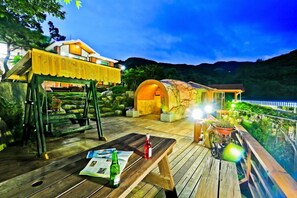 Una terraza de madera con una mesa, un columpio y un área de descanso cubierta con vistas a las montañas.