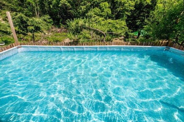 Una piscina azul cristalina rodeada por una valla de madera y abundante vegetación.