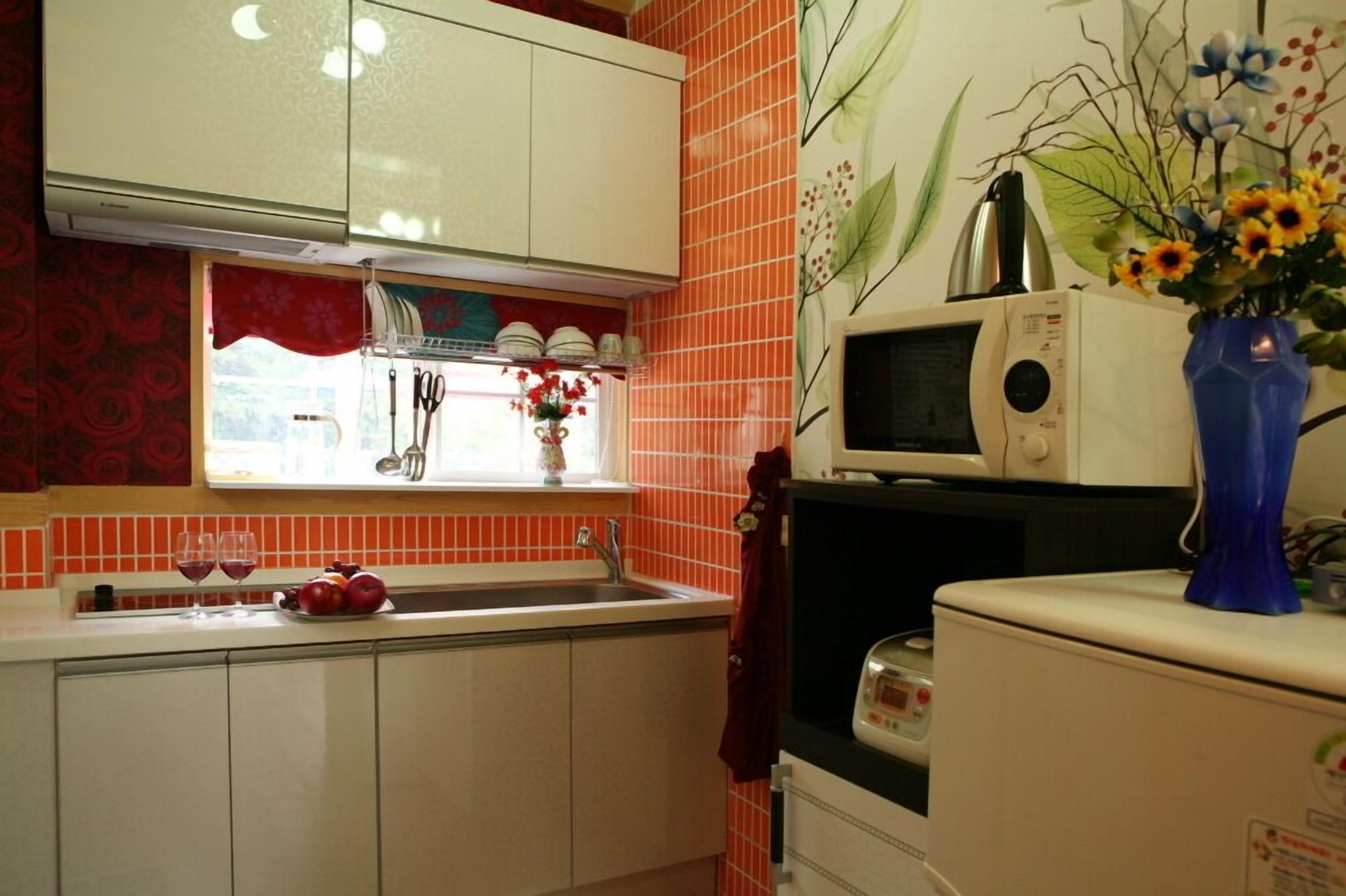 Una cocina con armarios blancos, salpicadero de baldosas rojas, un microondas y un jarrón con flores en la encimera.