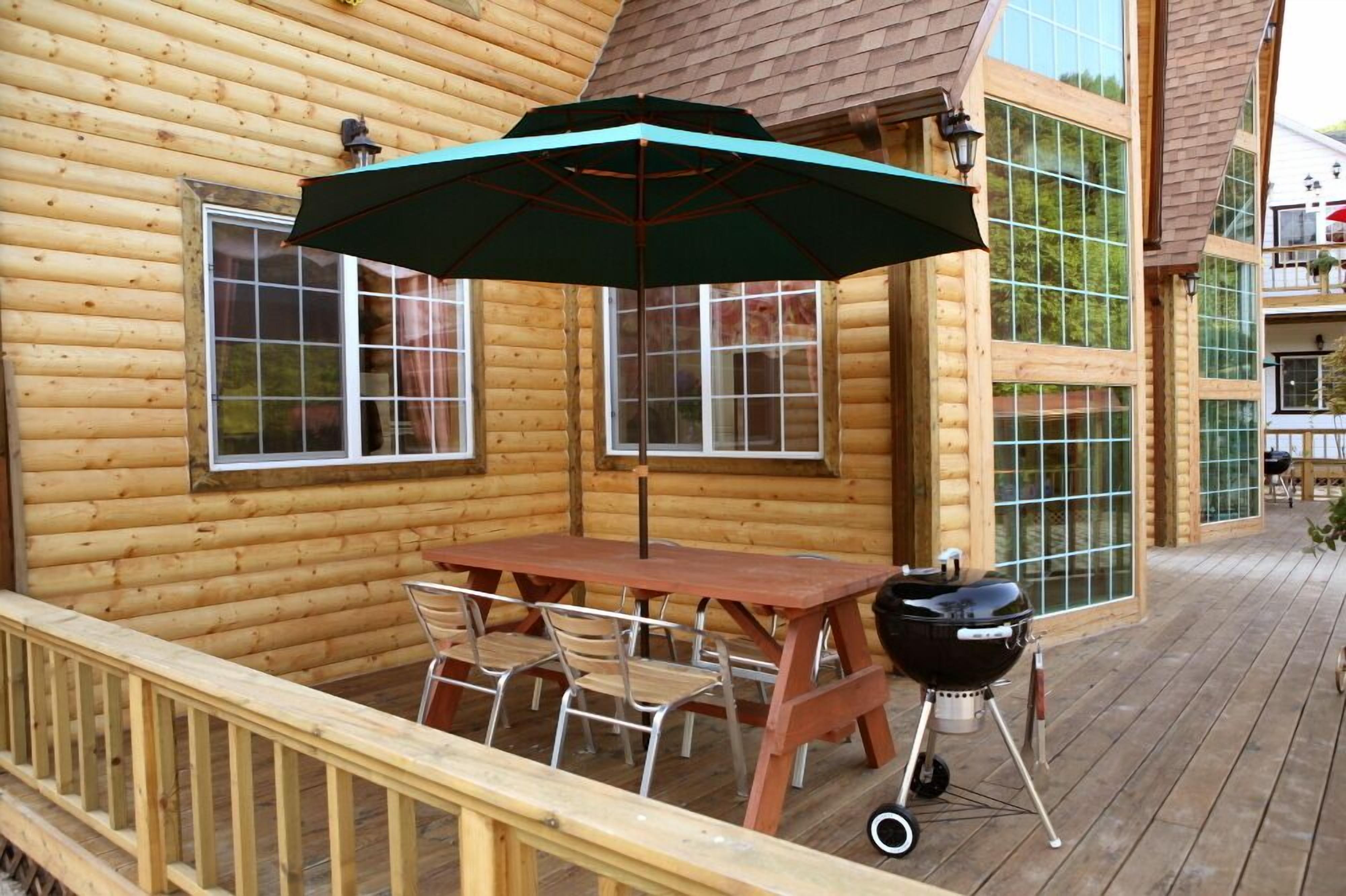 A wooden deck with a table and chairs, a barbecue grill, and a large umbrella.