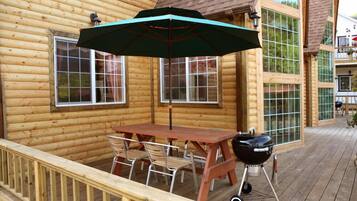 A wooden deck with a table and chairs, a barbecue grill, and a large umbrella.
