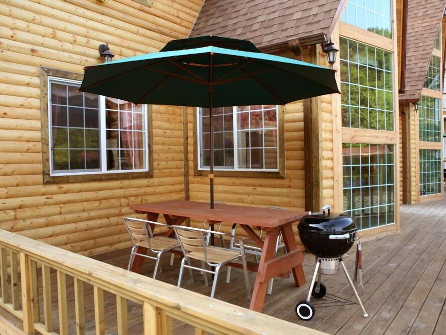 A wooden deck with a table and chairs, a barbecue grill, and a large umbrella.