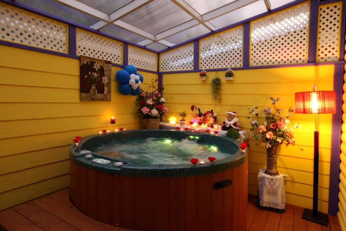 Uma banheira de hidromassagem cercada por flores decorativas e velas, com uma parede de madeira e um painel treliçado ao fundo.