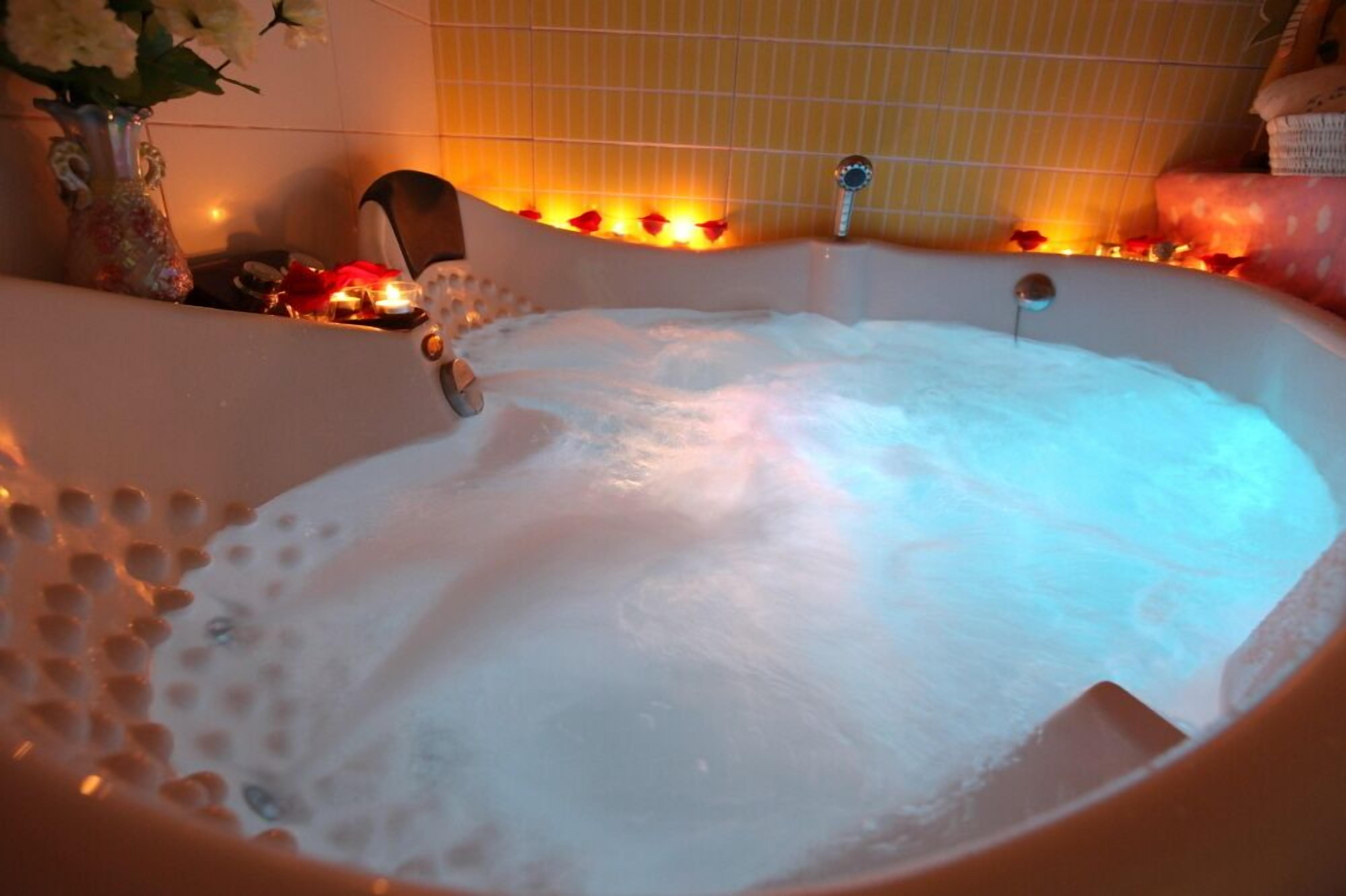 Une baignoire pleine de mousse, un vase avec des fleurs et un mur carrelé en arrière-plan.
