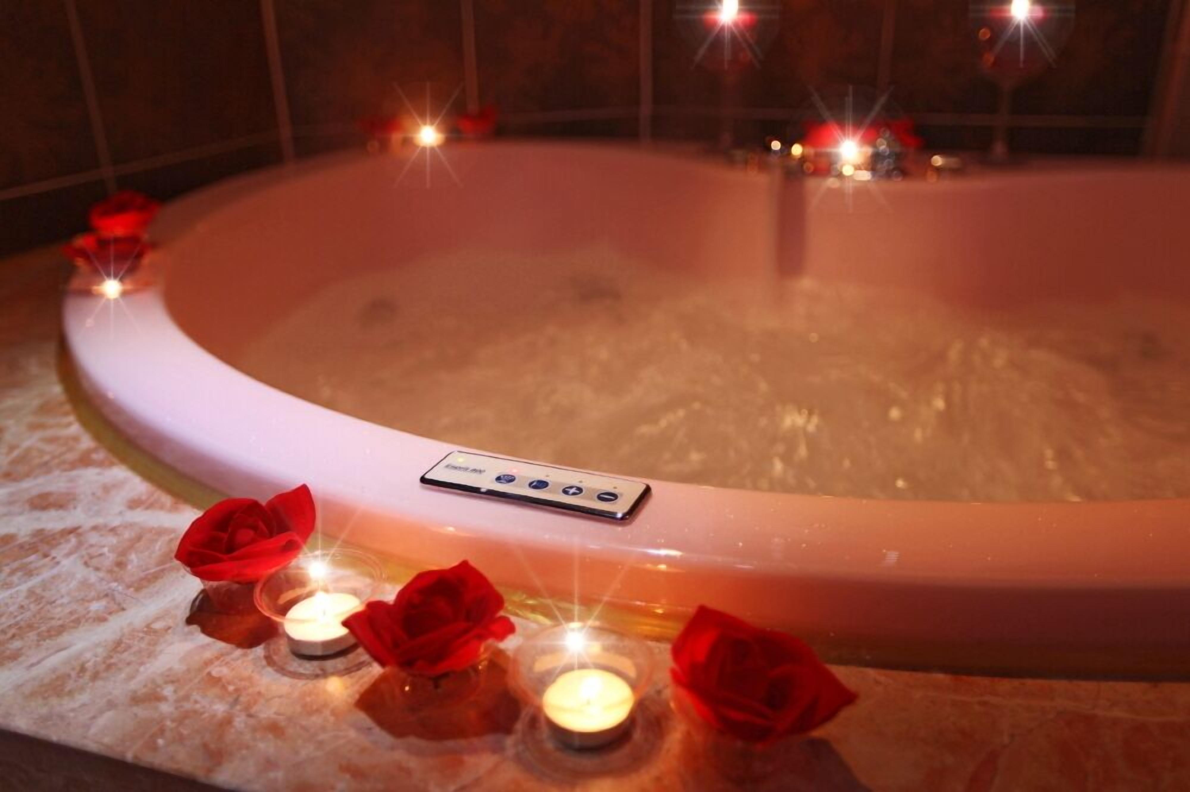 Un bain à remous doté d’un panneau de commande, entouré de bougies et de roses rouges.