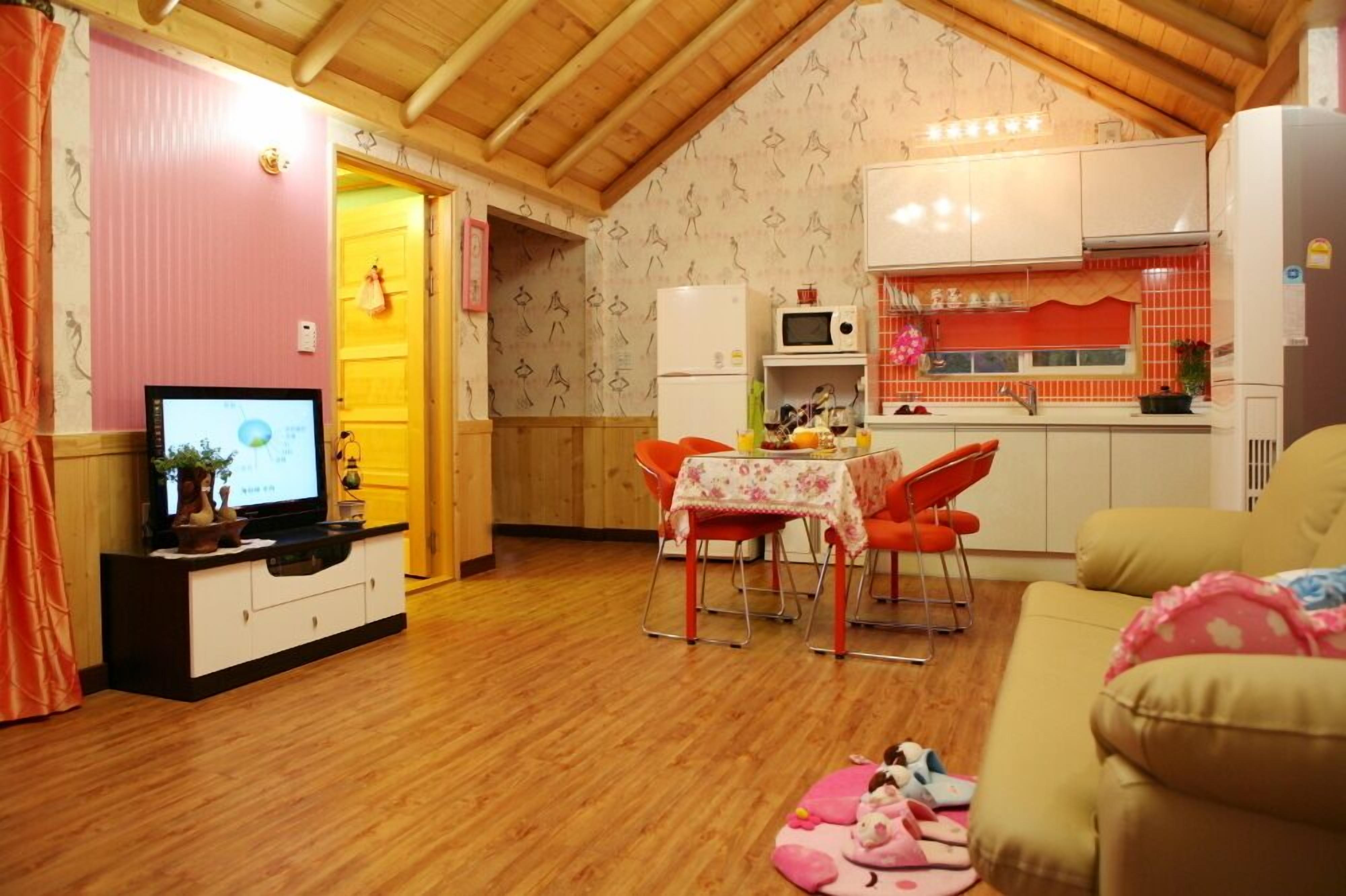 Un salon confortable avec un téléviseur, un plancher en bois, un coin repas avec une table et des chaises, et une cuisine équipée d’un four à micro-ondes et d’un réfrigérateur.