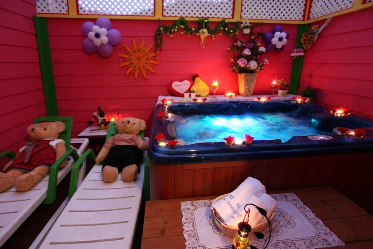 Quarto com banheira de hidromassagem, duas cadeiras verdes, um urso de pelúcia e uma mesa pequena com um urso de pelúcia em cima.
