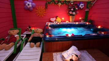 Ein Zimmer mit Whirlpool, zwei grüne Stühle, einem Teddybären und einem kleinen Tisch, auf dem ebenfalls ein Teddybär liegt.