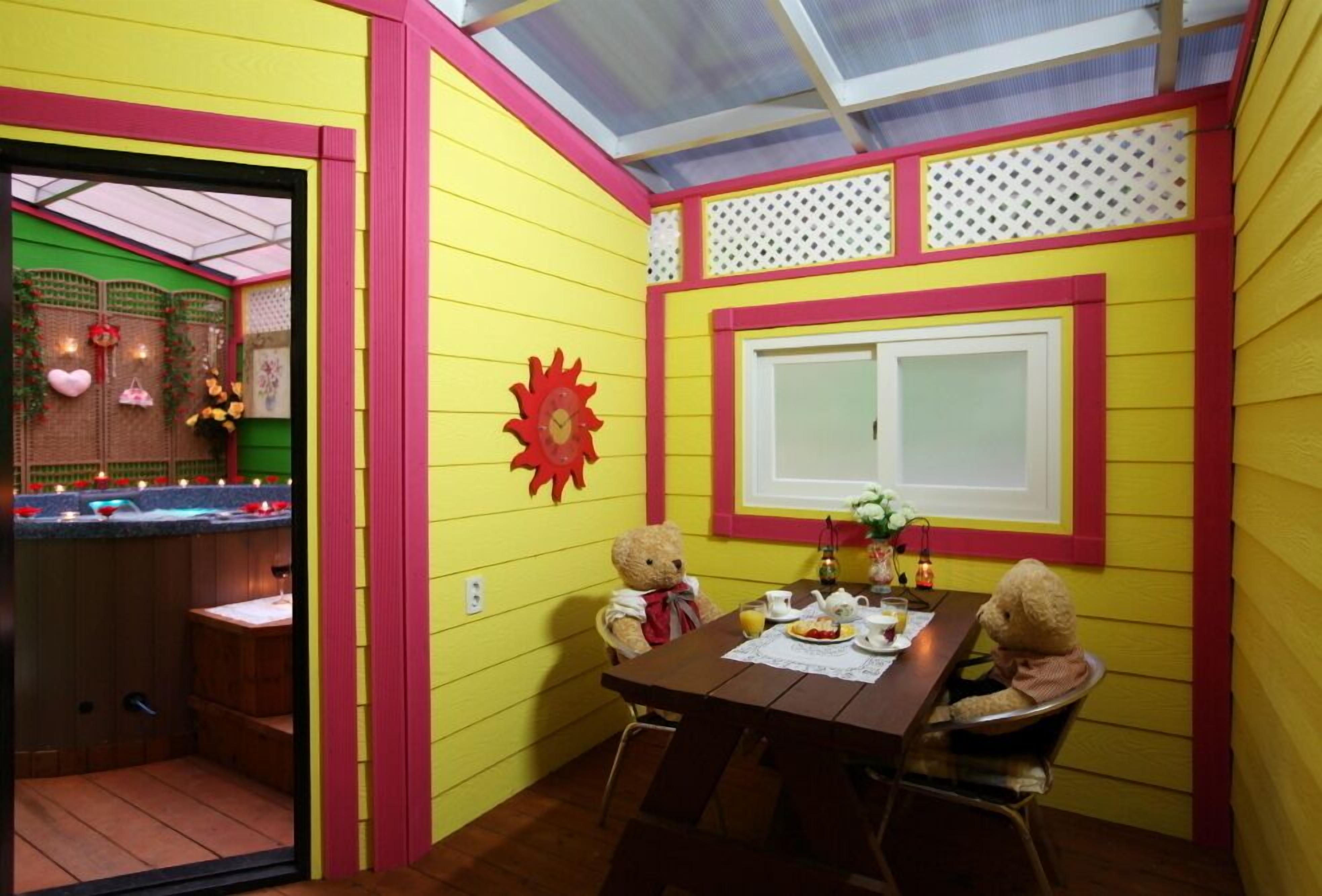 A room with yellow walls, a wooden table, two teddy bears, a window, and a sun-shaped decoration.