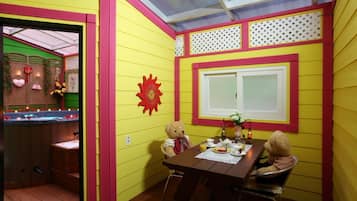 A room with yellow walls, a wooden table, two teddy bears, a window, and a sun-shaped decoration.