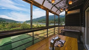 A room with large windows overlooking a scenic landscape, a wooden table, and a brick fireplace. - Milky Way Pension (Gapyeong)
