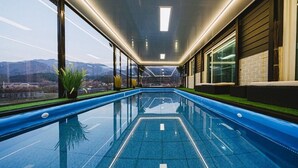 An indoor swimming pool with a view of mountains through large windows. - Milky Way Pension (Gapyeong)