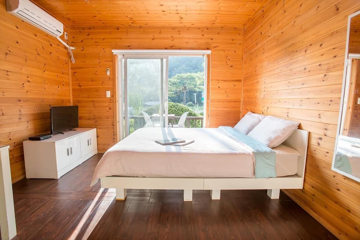 A wooden-paneled bedroom with a bed, a TV on a cabinet, and a large window.