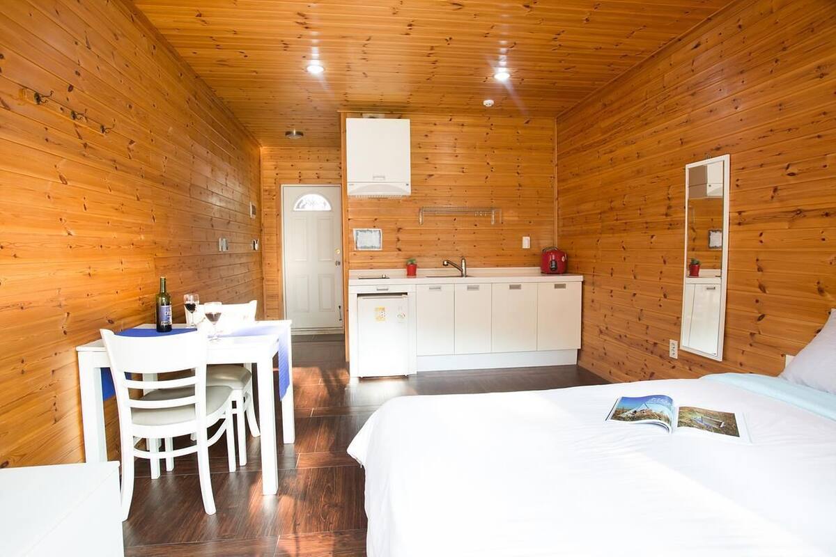 A wooden-paneled room with a bed, a table with chairs, a small kitchenette, and a mirror.