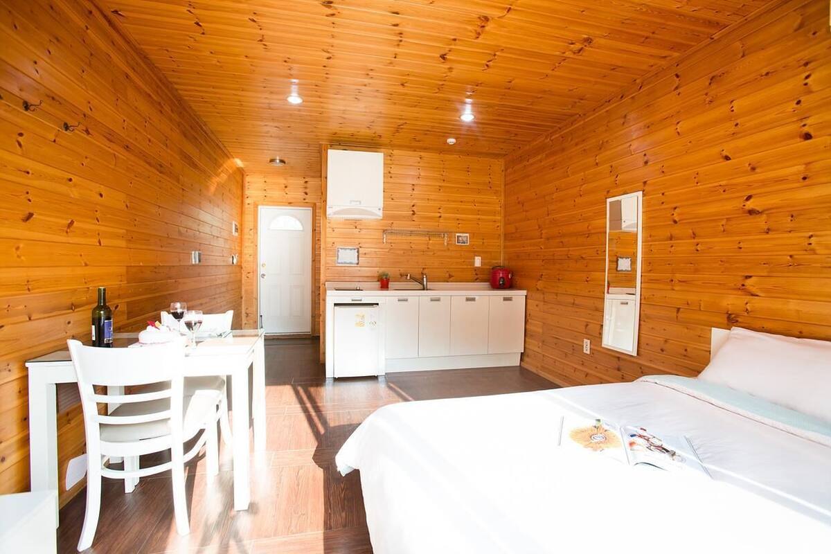 A wooden cabin with a dining area, kitchenette, and a bed.