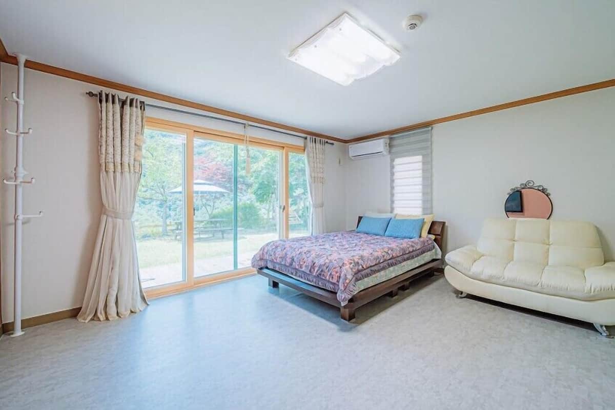 A bedroom with a bed, a sofa, a large window, and a ceiling light.