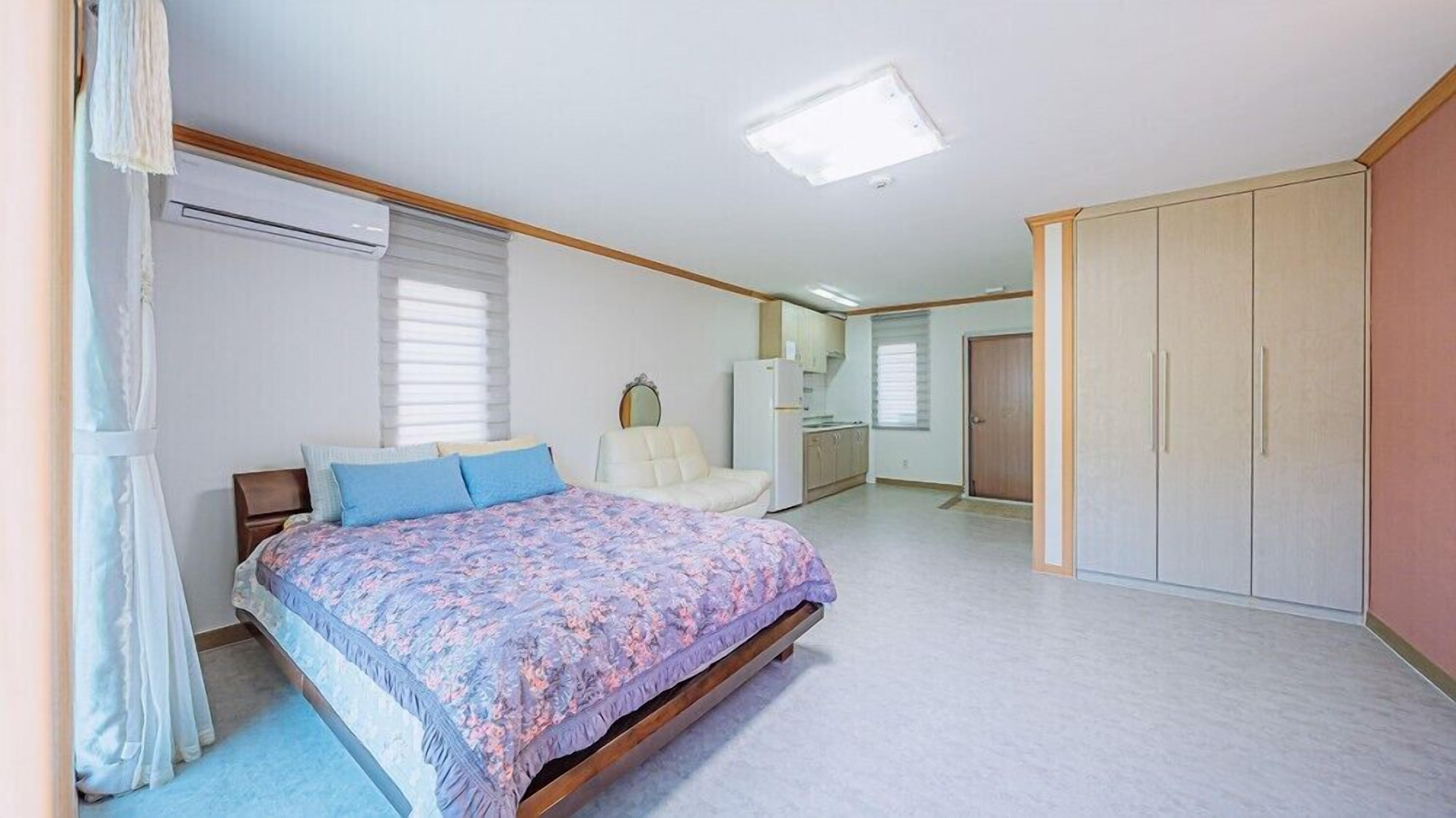 Une chambre comprenant un lit, une chaise, une armoire et un coin cuisine.