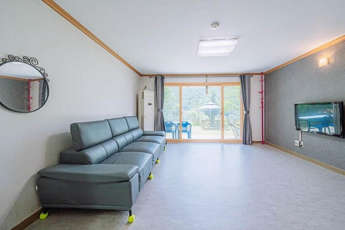 A modern living room with a grey sectional sofa, a flat-screen TV mounted on the wall, and a sliding glass door leading to an outdoor area.