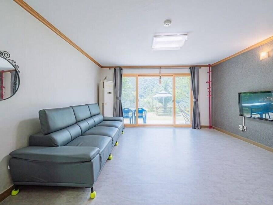 A modern living room with a grey sectional sofa, a flat-screen TV mounted on the wall, and a sliding glass door leading to an outdoor area.