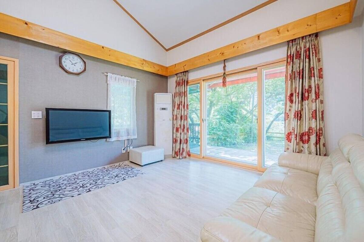 A living room with a sofa, a TV, a clock, and a window with curtains.