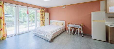 Un dormitorio con una cama, una mesita con sillas, un refrigerador y una ventana con cortinas.